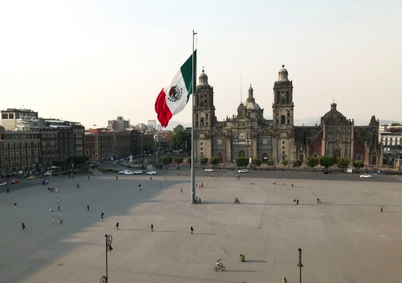 Personas caminan alrededor de la bandera mexicana en el Zócalo en la Ciudad de México, que luce con pocas personas en medio del brote de coronavirus. 25 de marzo de 2020. REUTERS/Henry Romero