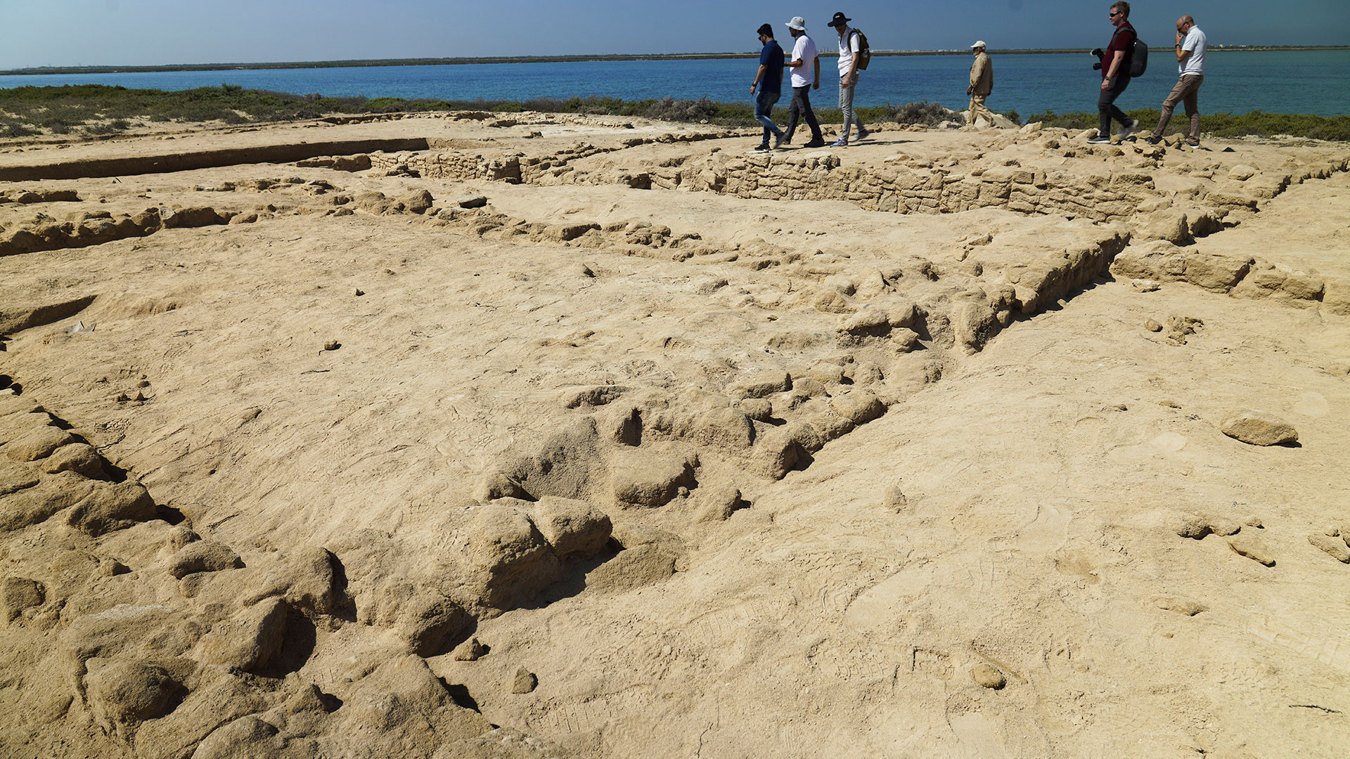 Arqueólogos y periodistas caminan frente a ruinas descubiertas en la isla de Siniyah en Umm al-Quwain, Emiratos Árabes Unidos, el lunes 20 de marzo de 2023.  (Foto AP/Jon Gambrell)

