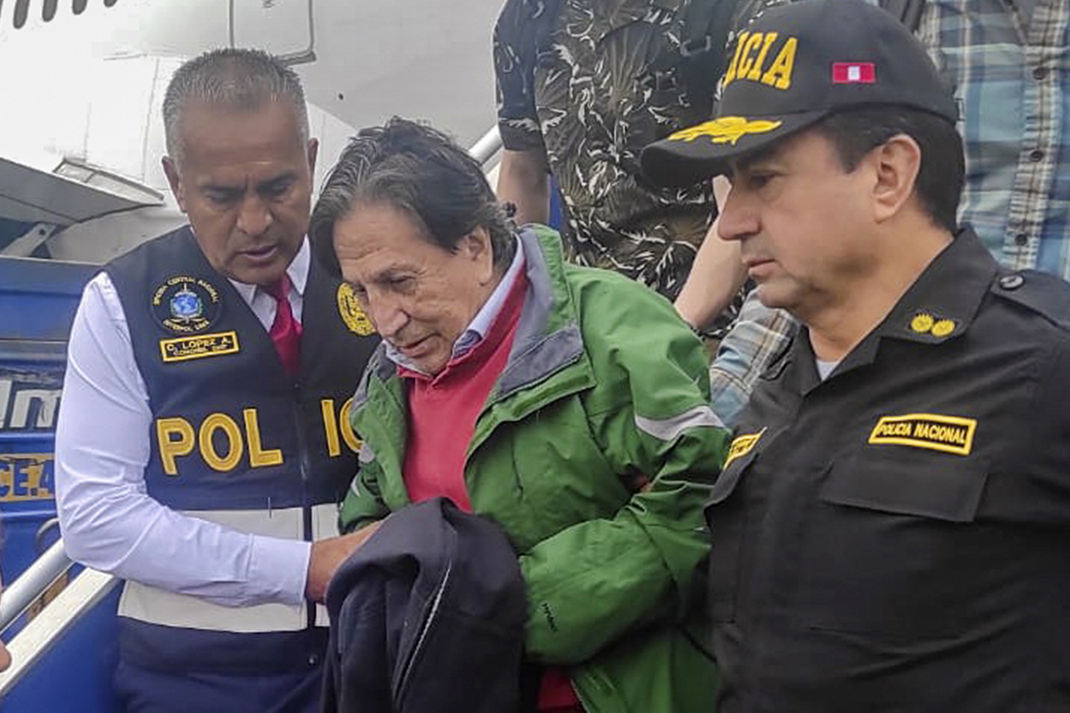 En esta foto difundida por la Policía Nacional de Perú, agentes escoltan al expresidente Alejandro Toledo a su llegada, extraditado desde Estados Unidos, al aeropuerto de Lima, el domingo 23 de abril de 2023. (Policía Nacional de Perú vía AP)