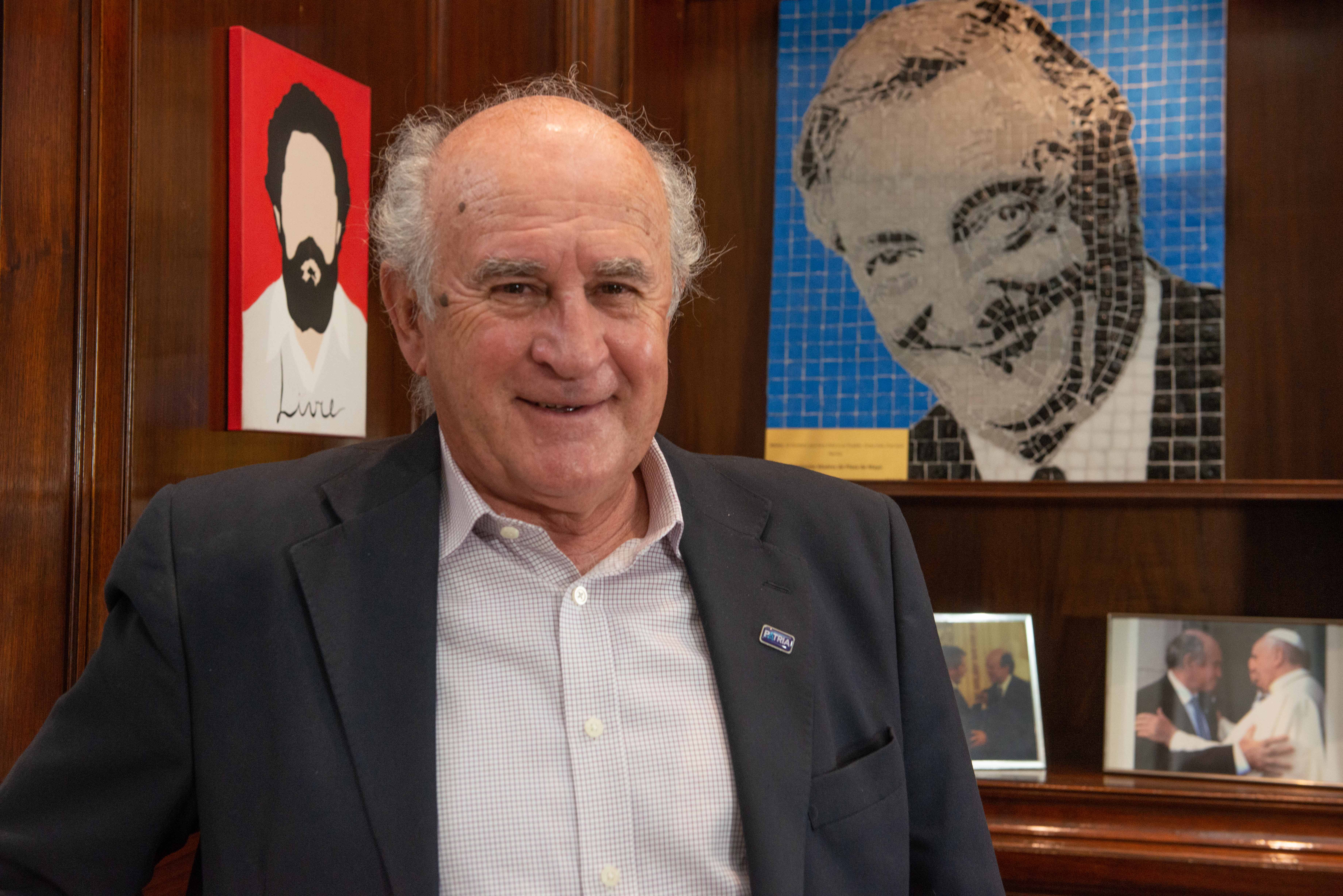 Oscar Parrilli sonríe en su despacho en el Senado; de fondo, un cuadro de Néstor Kirchner y su foto con el papa Francisco (Foto: Gaston Taylor)